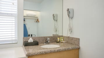 Baño con encimera de granito, lavabo, espejo y secador de pelo fijado a la pared.