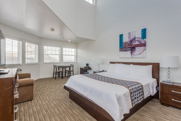 A hotel room with a large bed, a desk, a chair, and a dining table. - Pacifica Beach Hotel (Pacifica)