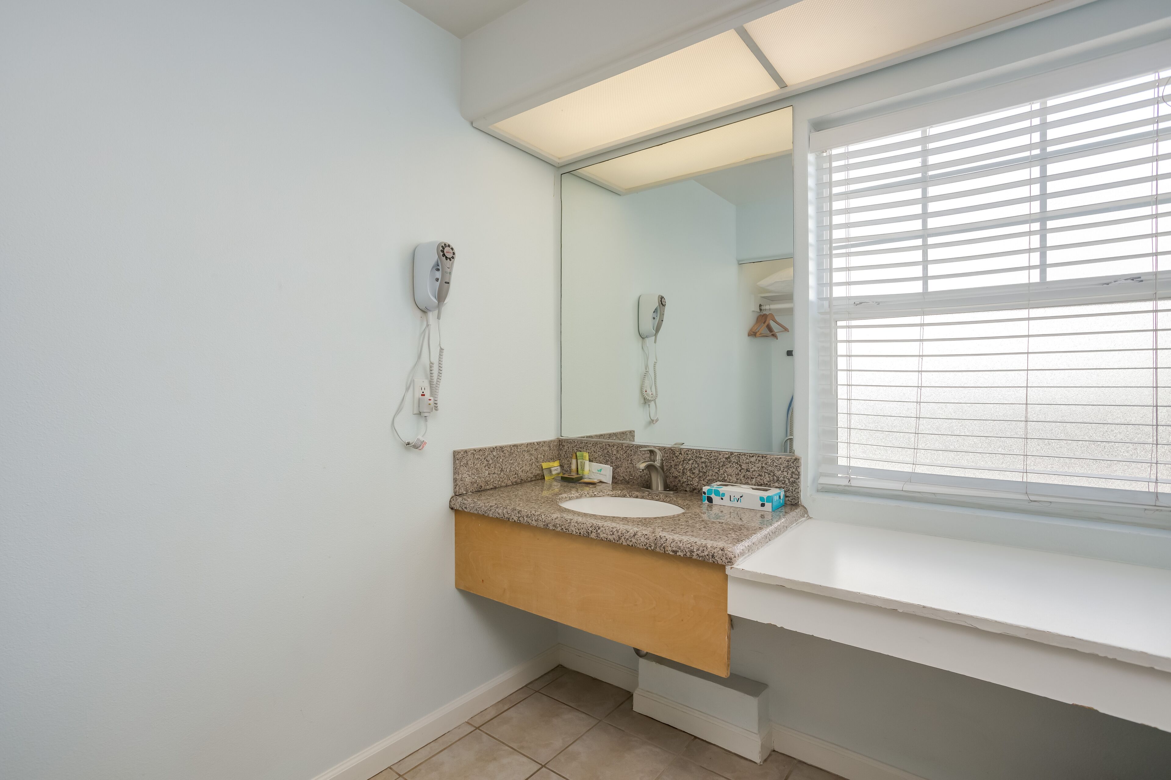 A bathroom with a white sink, a mirror, and a hairdryer mounted on the wall.