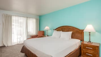 Ein Hotelzimmer mit einem großen Bett, zwei Nachttischen mit Lampen, einem Sessel und einem Fenster mit Vorhängen.