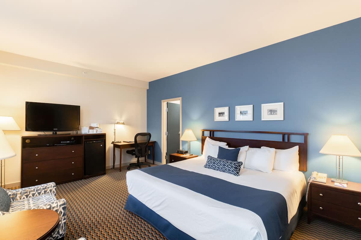A hotel room with a bed, desk, chair, TV, and bedside tables.