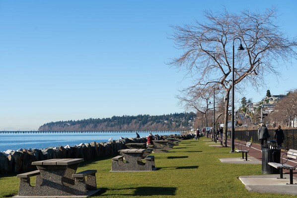 A park with picnic tables, benches, and a walking path along a waterfront.