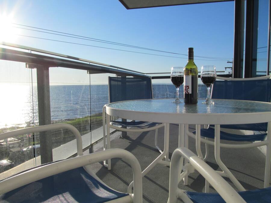 A balcony with a table, chairs, a bottle of wine, and two wine glasses.