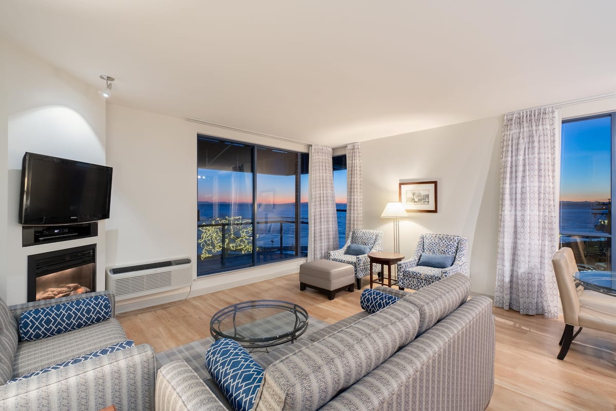 A modern living room with a large window, a flat-screen TV, and a fireplace.