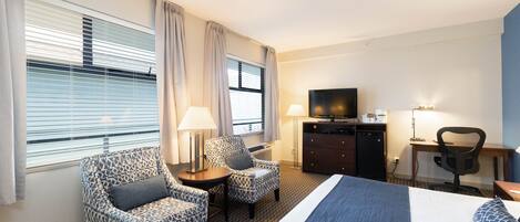 A hotel room with a large bed, two patterned armchairs, a desk with a television, and a dresser.