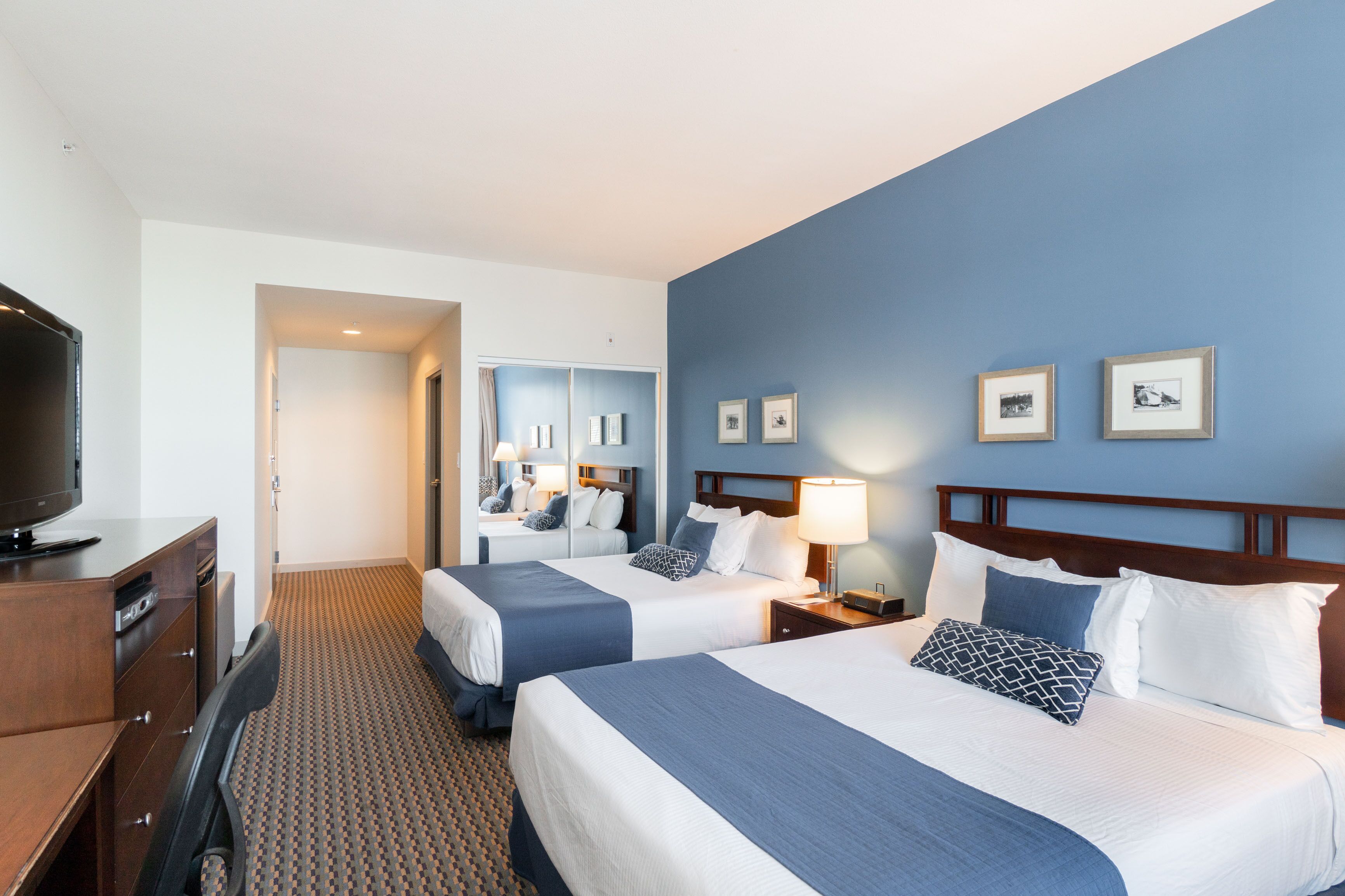 A hotel room with two beds, a TV, a desk, and a mirror.