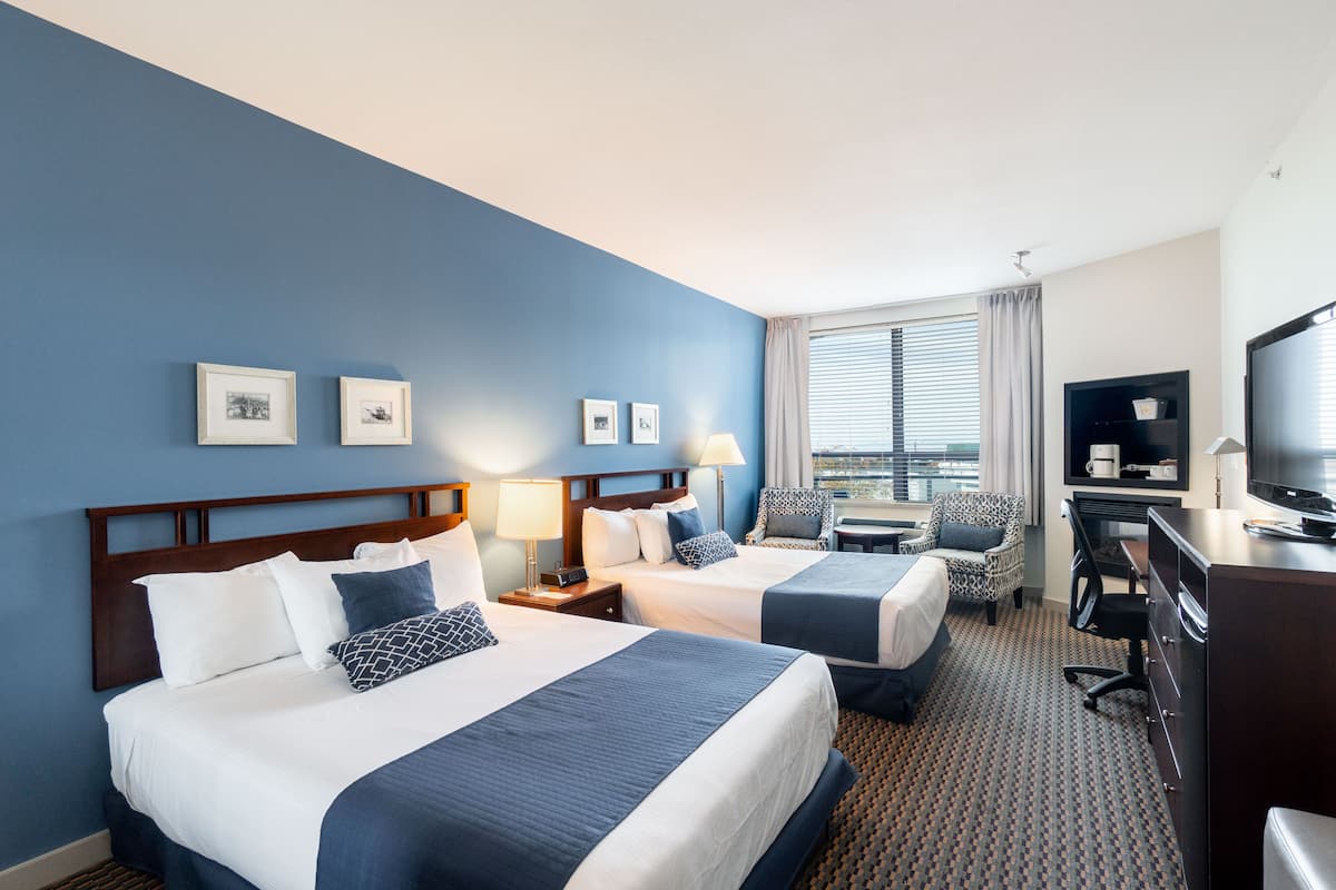 A hotel room with two beds, a desk, a chair, a television, and a window with blinds.