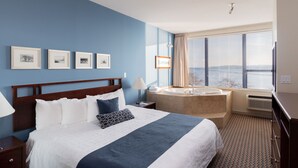 A hotel room with a large bed, a bathroom with a bathtub, and a window with blinds.