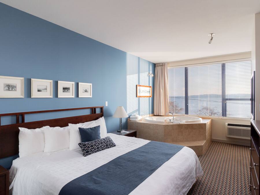 A hotel room with a large bed, a bathroom with a bathtub, and a window with blinds.