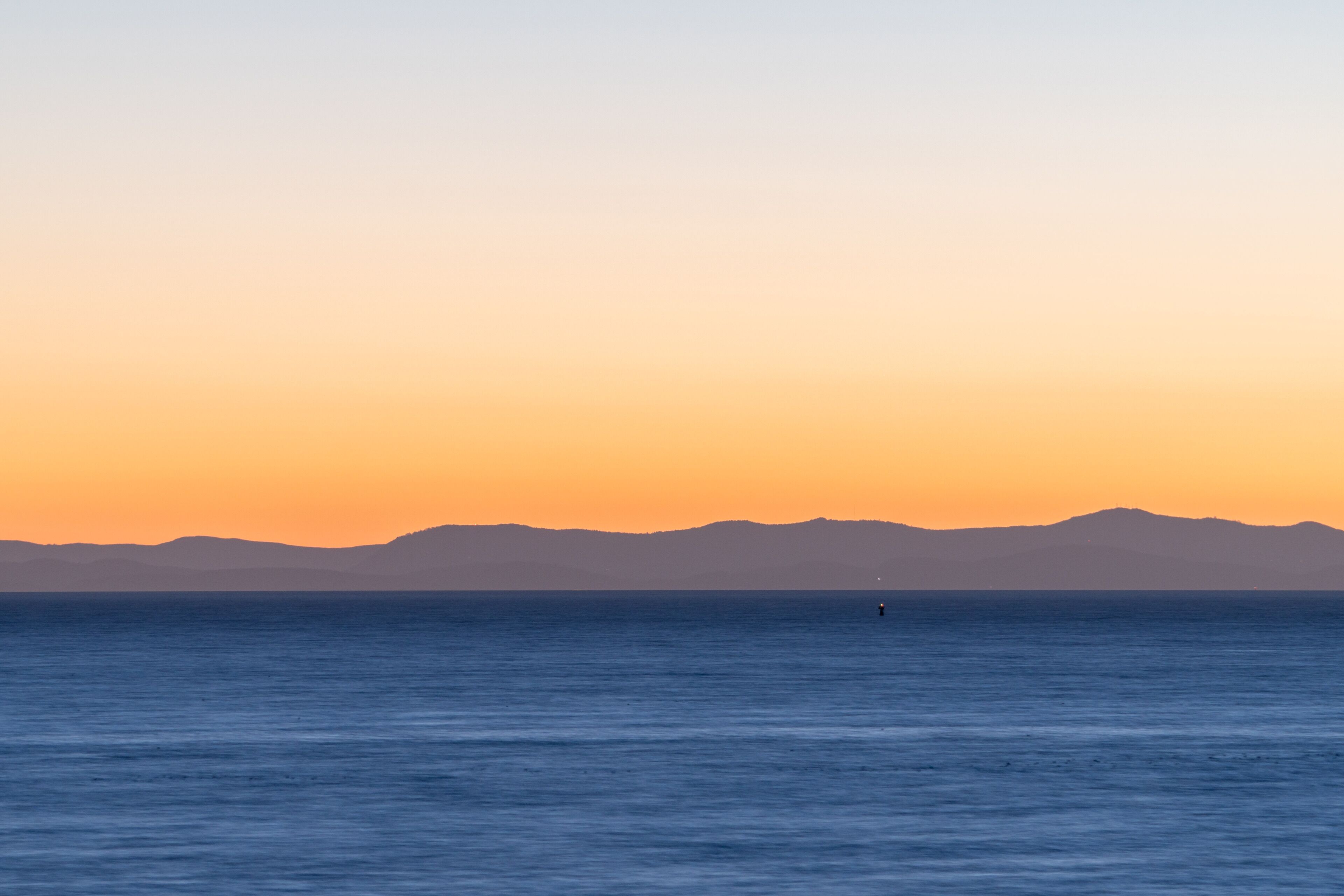 Mar tranquila al atardecer con montañas a lo lejos.
