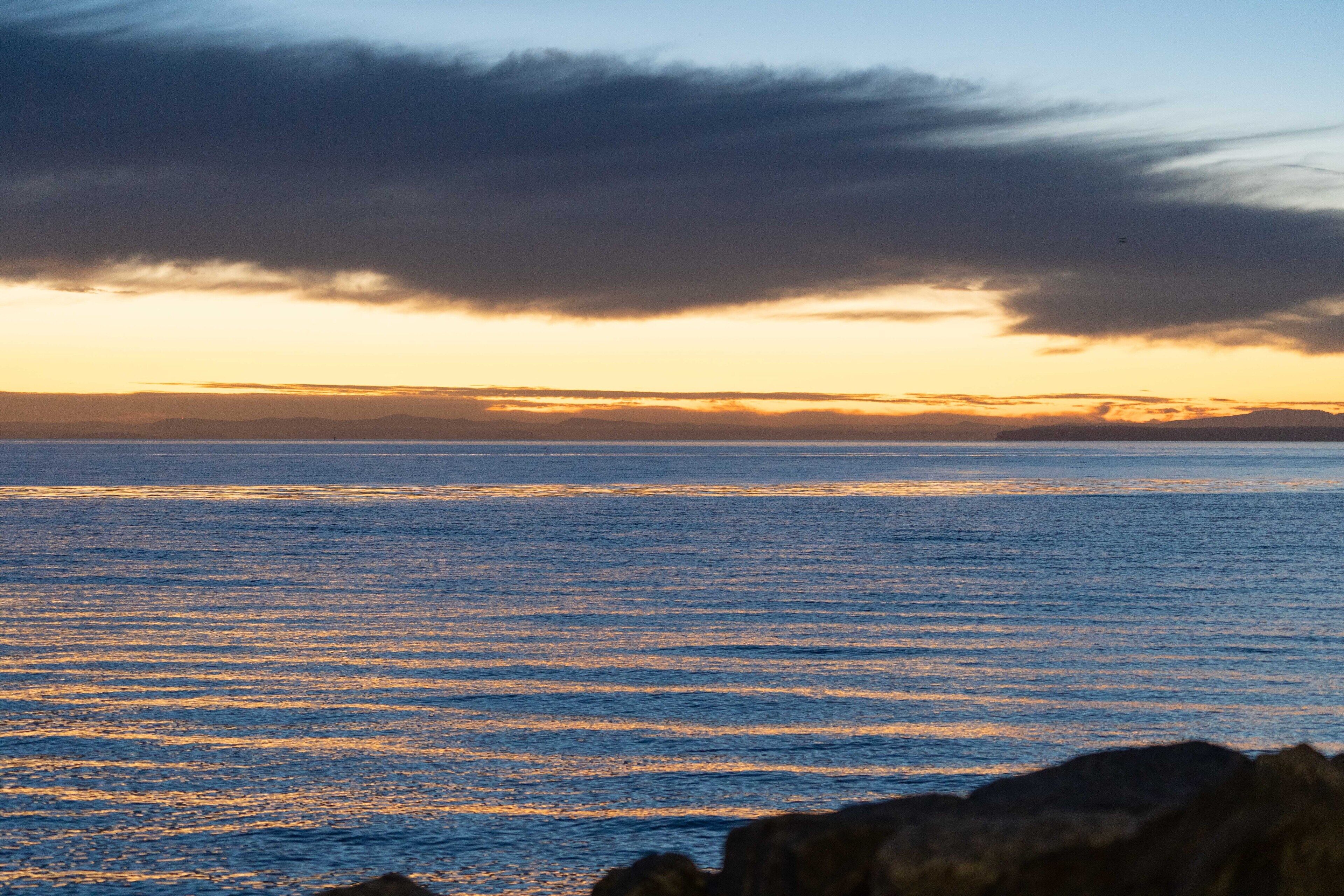 A coastal sunset with a calm sea and rocky foreground.