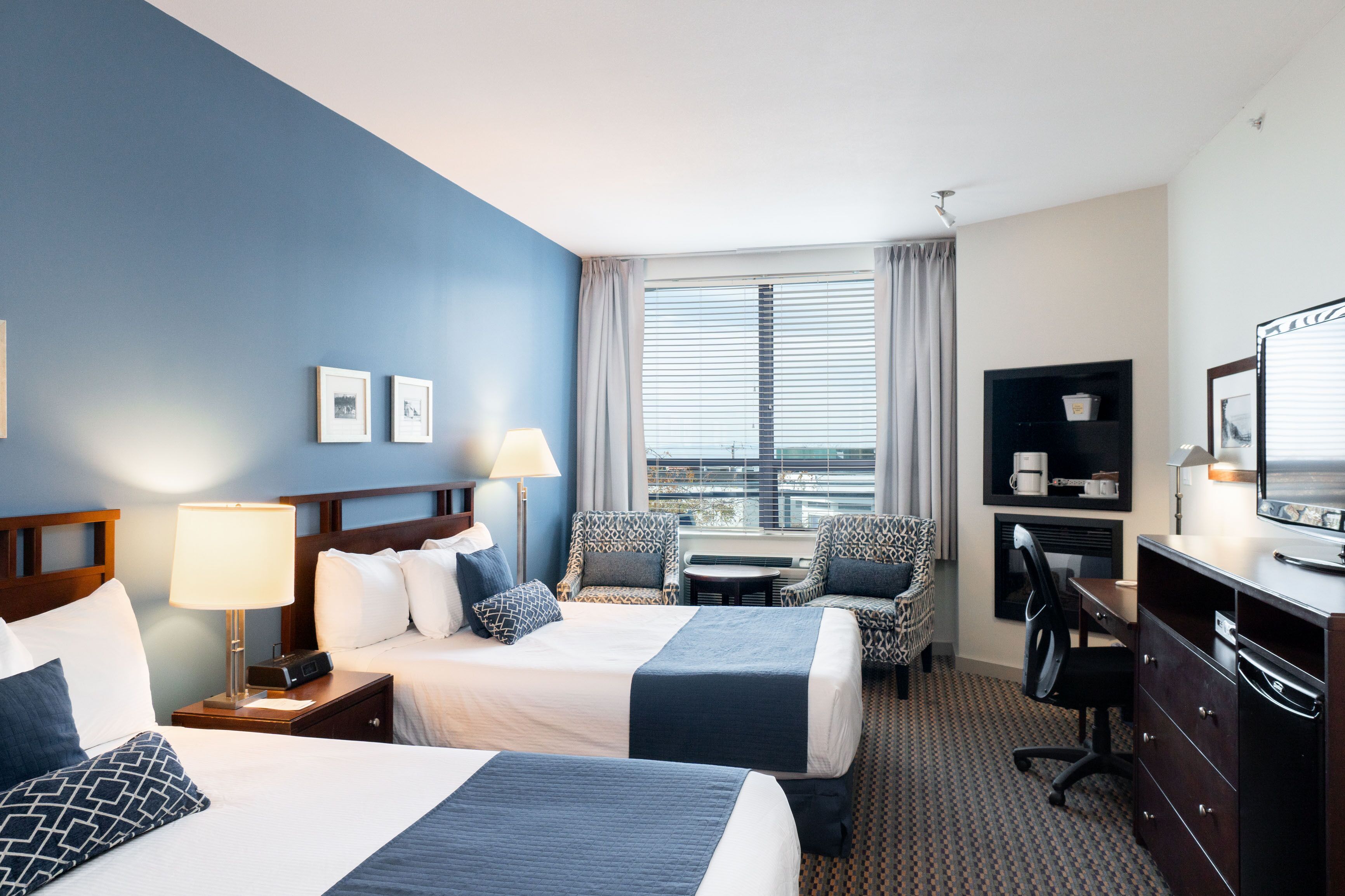 Hotelkamer met twee bedden, een bureau, een stoel, een televisie en een raam met gordijnen.