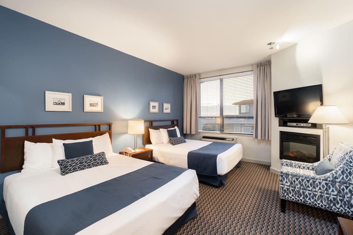 A hotel room with two beds, a TV, a fireplace, and a patterned armchair.