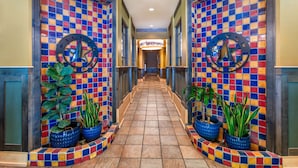 Un couloir aux murs ornés de mosaïques colorées, agrémenté de plantes en pot et surmonté d’un panneau central.