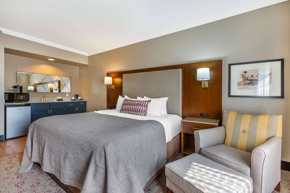 Een hotelkamer met een groot bed, een bureau met een lamp, een stoel en een lijst met een afbeelding aan de muur.