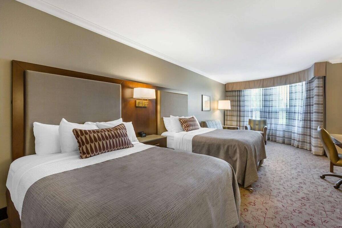 Een hotelkamer met twee bedden, een bureau, een stoel en een groot raam met gordijnen.