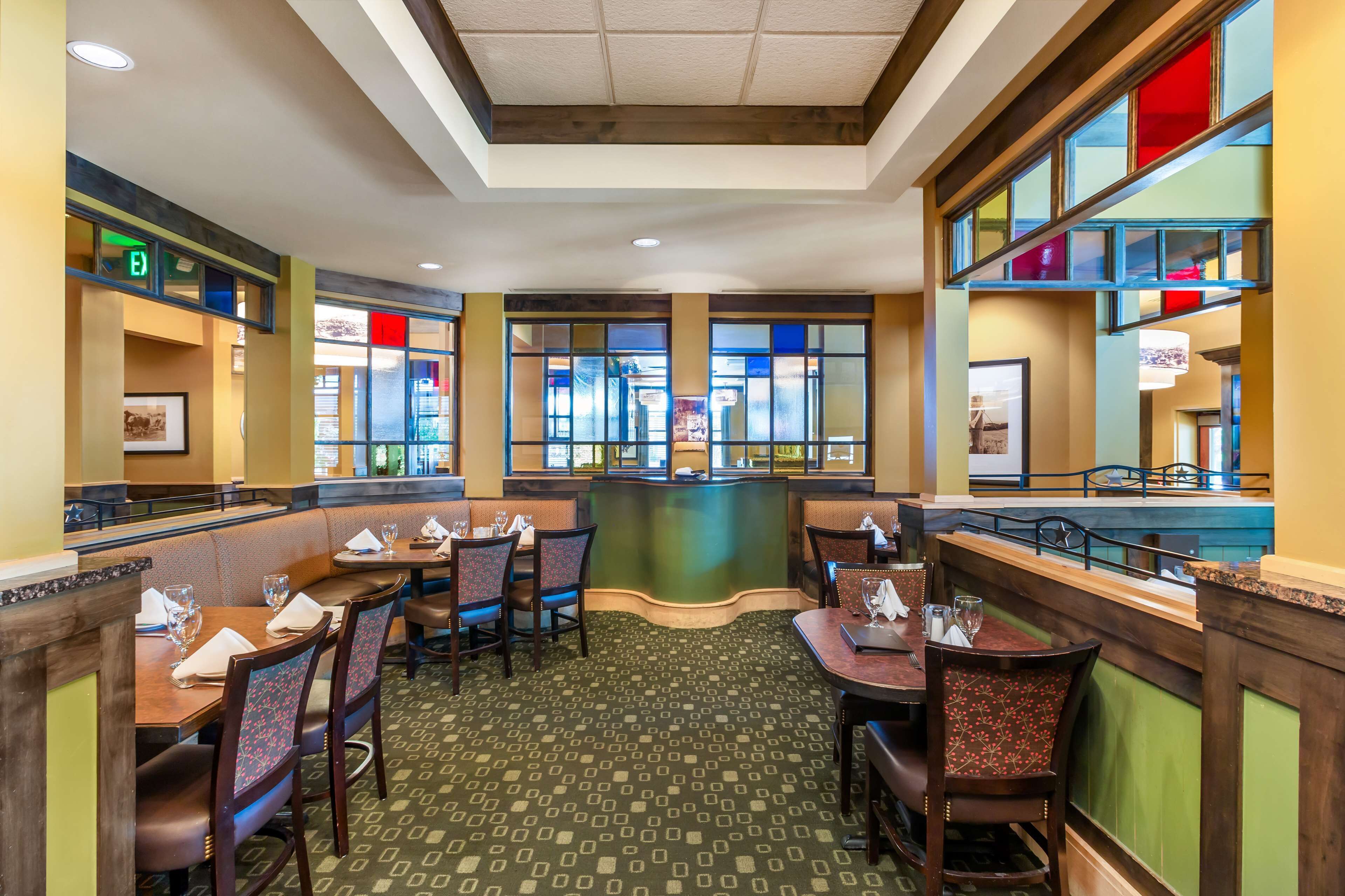 A restaurant with booths and tables, a patterned carpet, and a view through large windows.