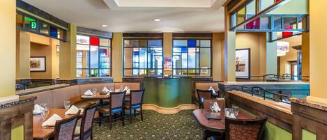 A restaurant with booths and tables, a patterned carpet, and a view through large windows.