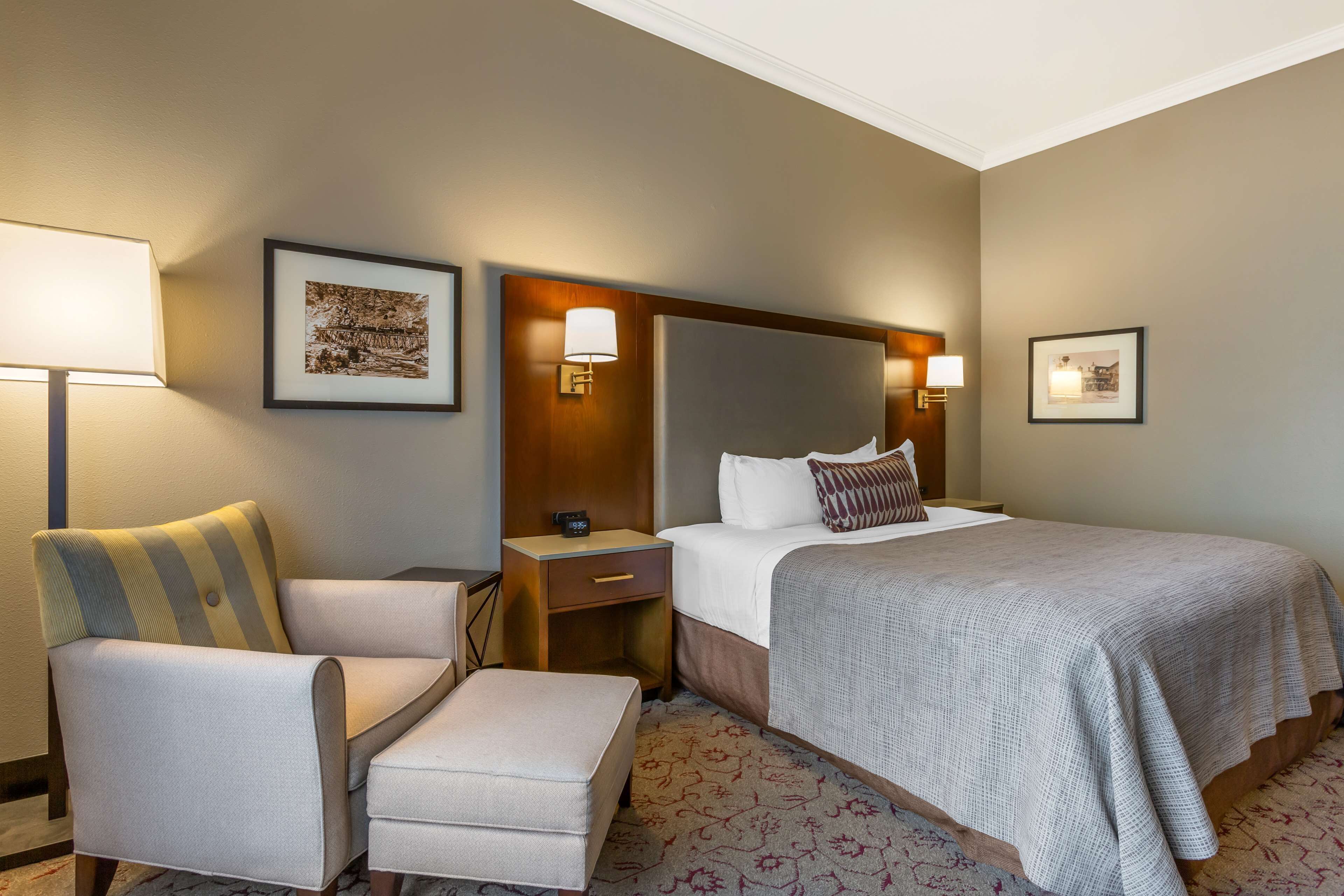 A hotel room with a large bed, a chair, a nightstand, and a wall-mounted lamp.