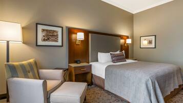 A hotel room with a large bed, a chair, a nightstand, and a wall-mounted lamp.