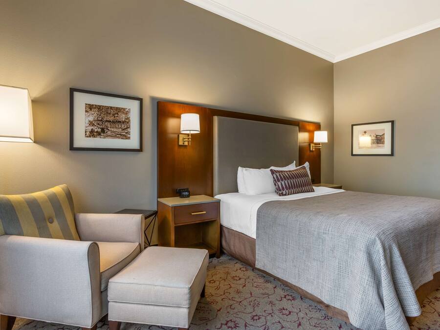 A hotel room with a large bed, a chair, a nightstand, and a wall-mounted lamp.