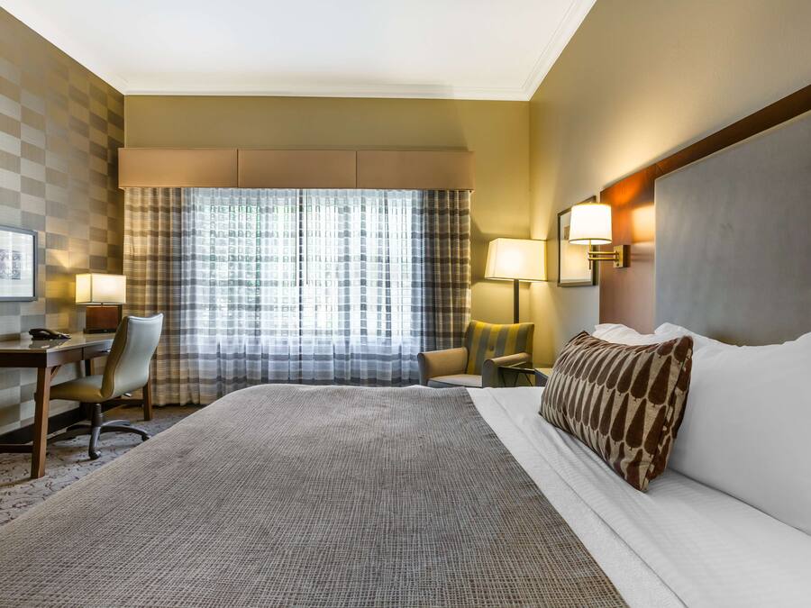 Hotelkamer met een groot bed, een bureau met stoel, een lamp en een raam met gordijnen.