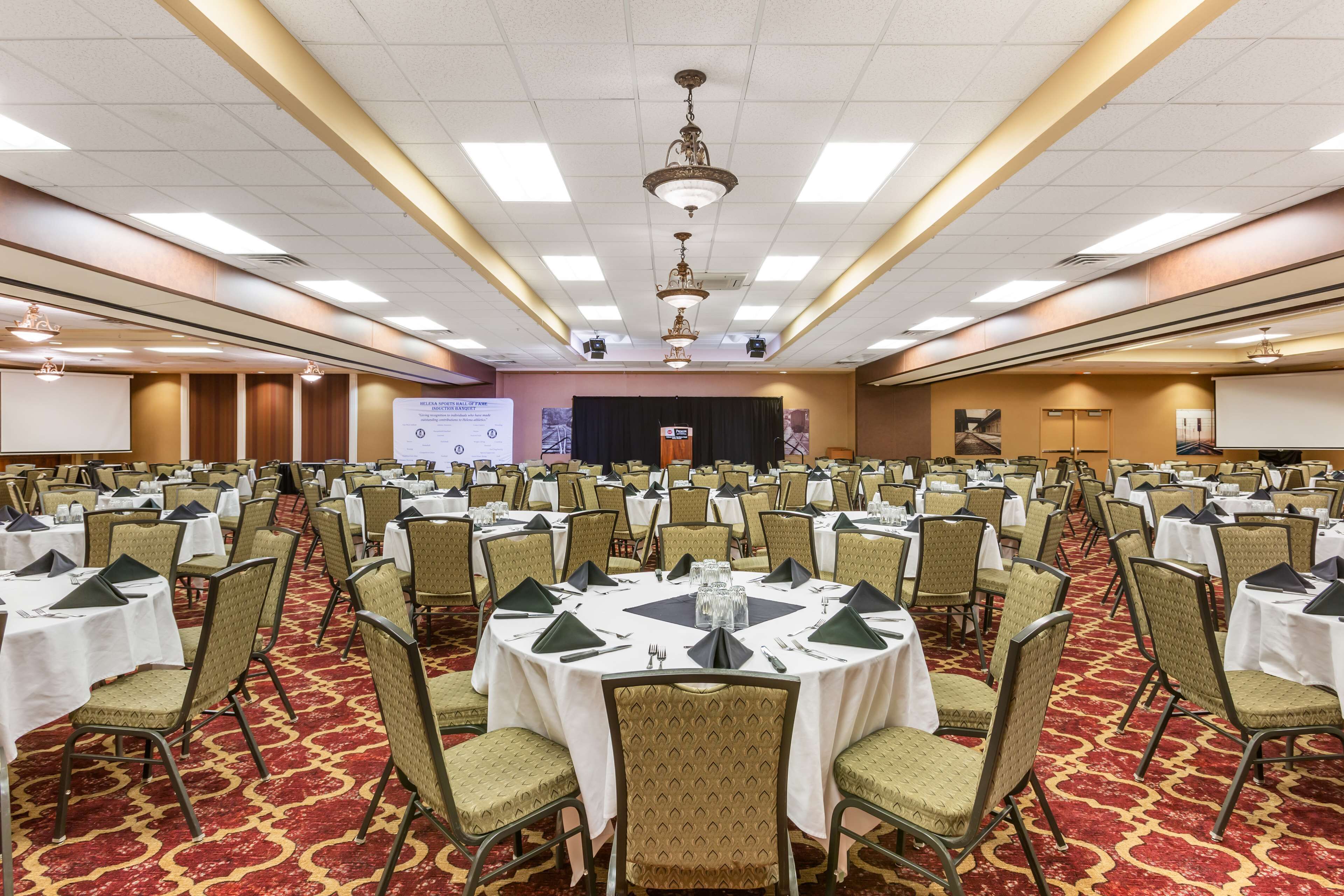A large conference room with round tables, chairs, and a stage with a presentation screen.