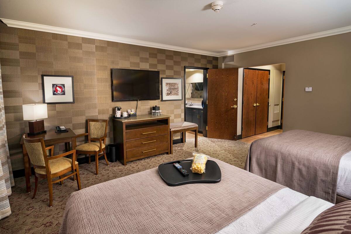 Een hotelkamer met twee bedden, een bureau met stoel, een televisie en een kledingkast.