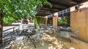 Un espace extérieur aménagé en terrasse, avec des tables et des chaises en métal, un coin salon abrité et une vue sur la rue.