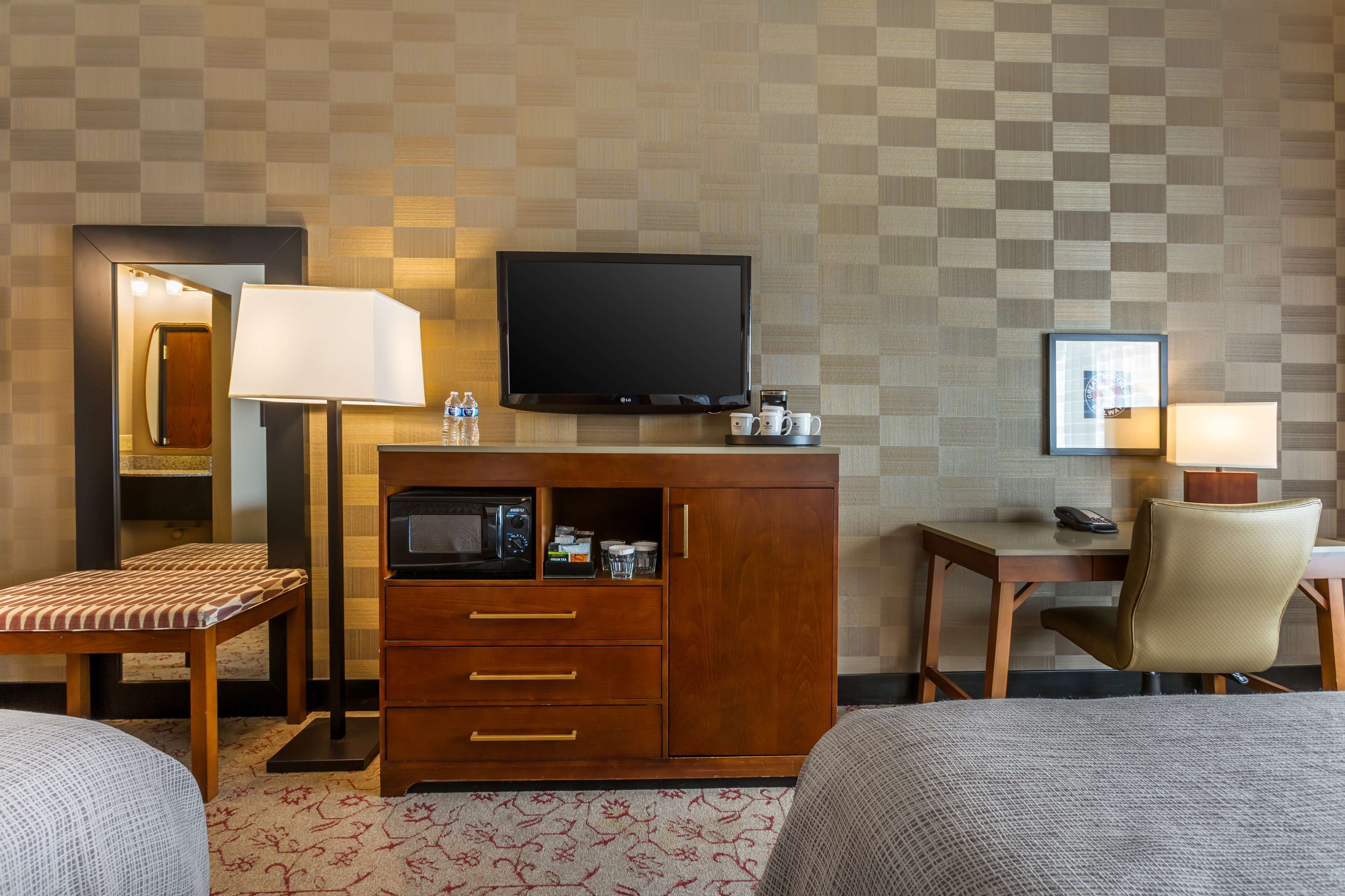 Une chambre d’hôtel équipée d’une télévision, d’un bureau avec une chaise, d’un lit et d’une petite armoire avec des tiroirs.