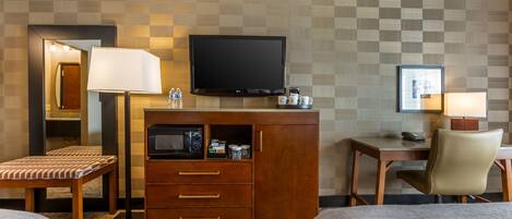 Une chambre d’hôtel équipée d’une télévision, d’un bureau avec une chaise, d’un lit et d’une petite armoire avec des tiroirs.