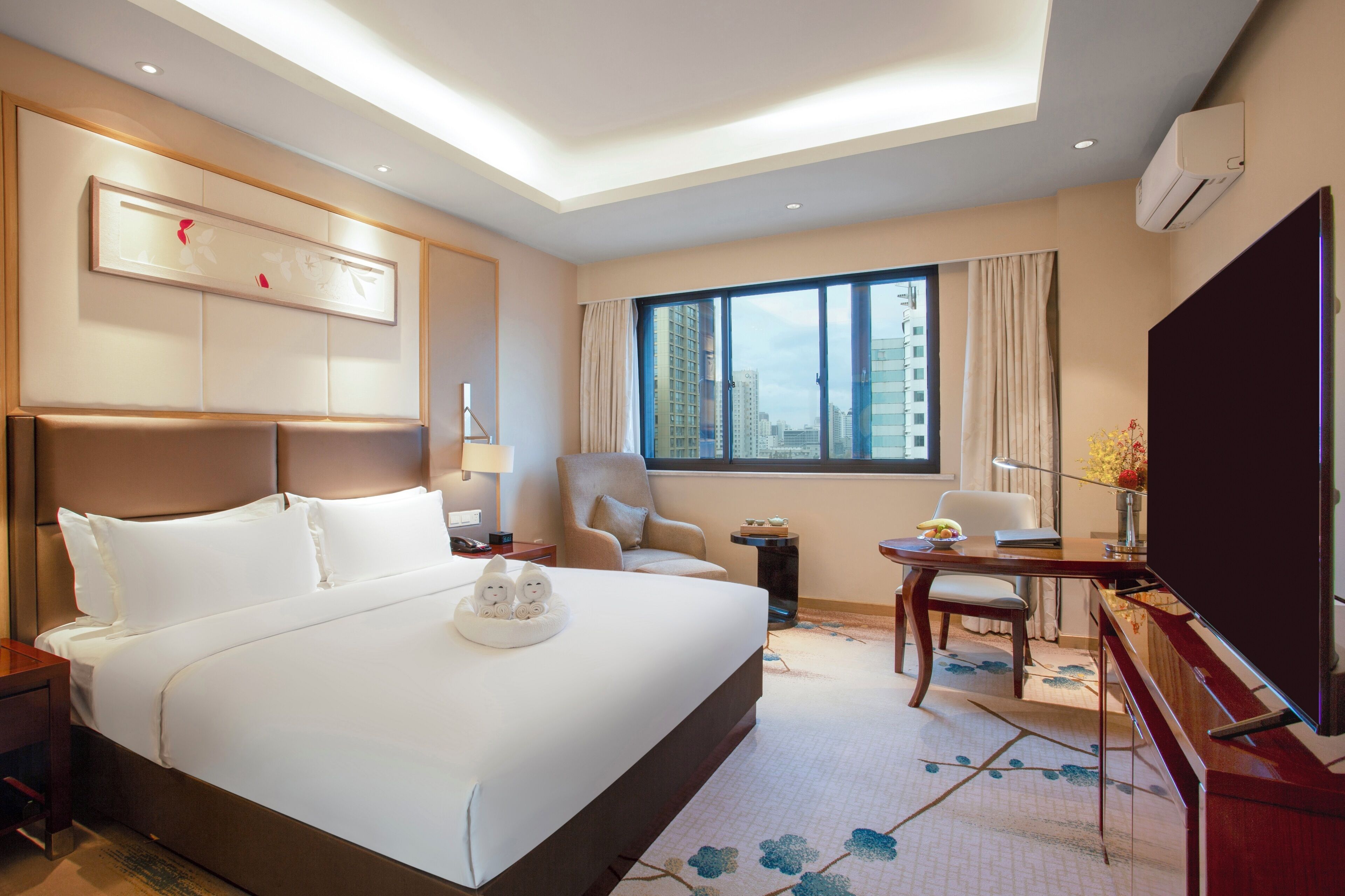 A hotel room with a large bed, a desk with a chair, a TV, and a window with curtains.