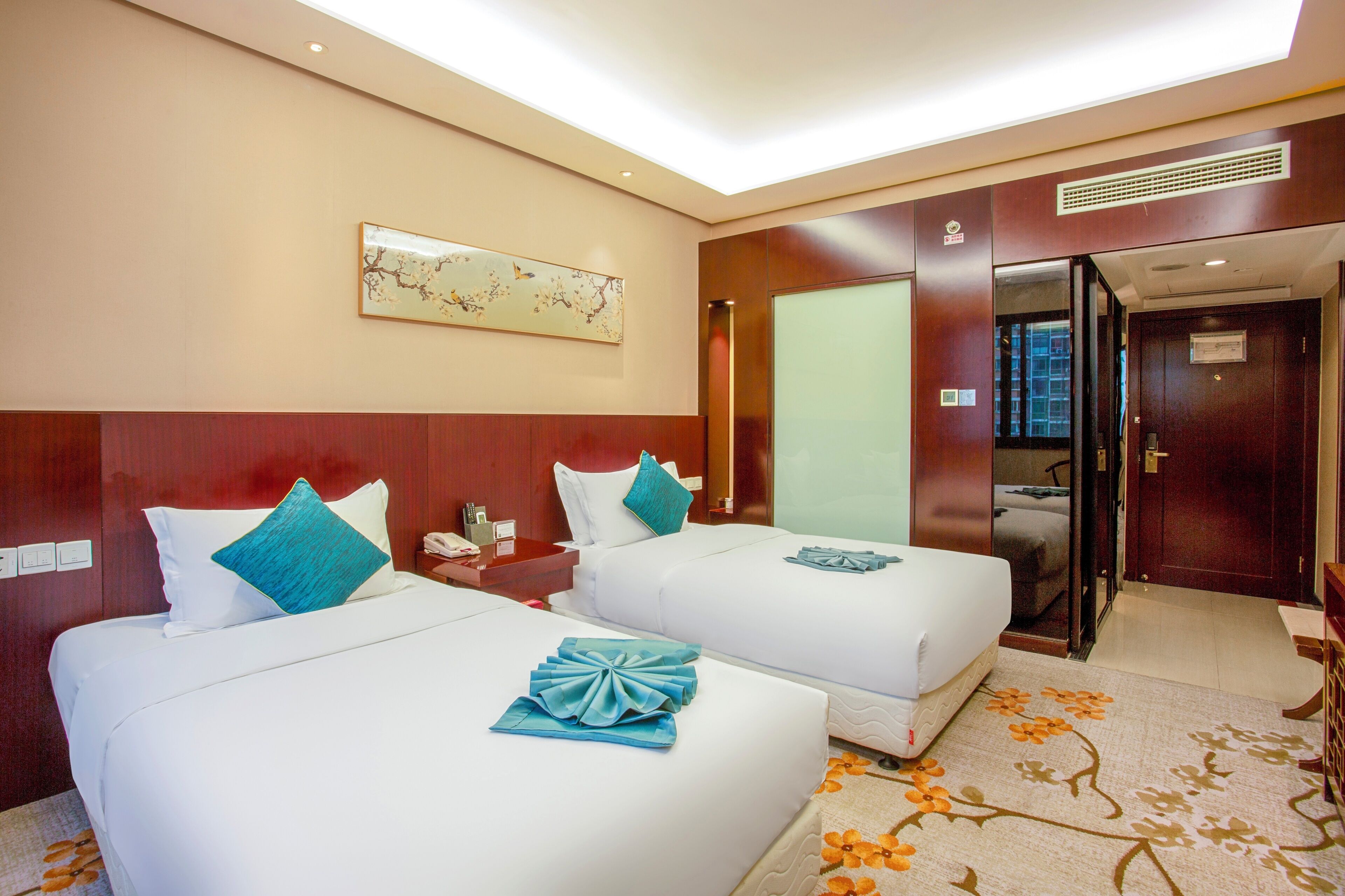 A hotel room with two beds, a nightstand, a desk, a chair, a mirror, and a door.