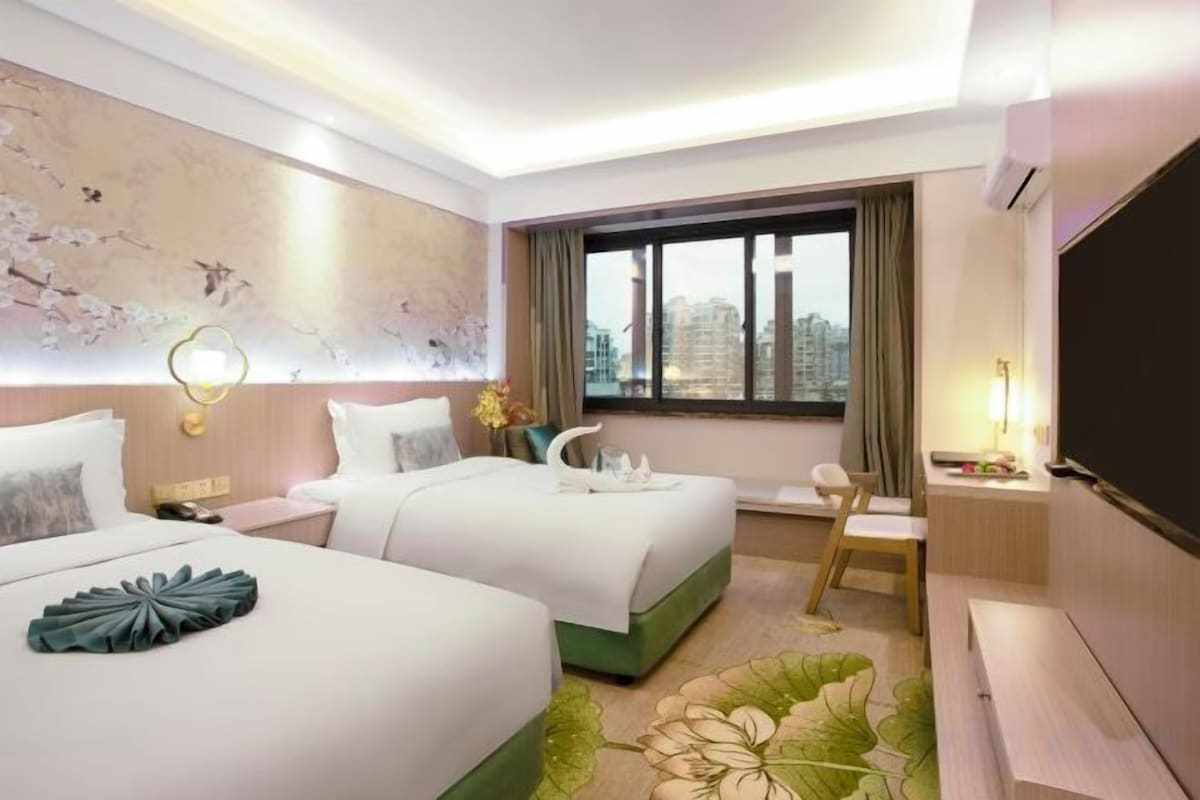 Une chambre d’hôtel avec deux lits, un bureau, une chaise, une télévision et une grande fenêtre donnant sur la ville.