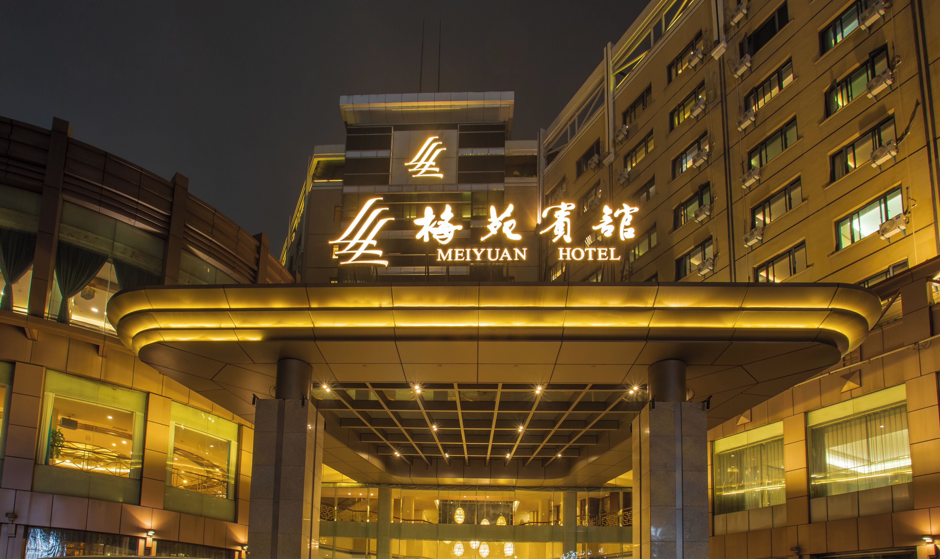A hotel entrance with a modern design, featuring a prominent illuminated sign and a covered entrance area.