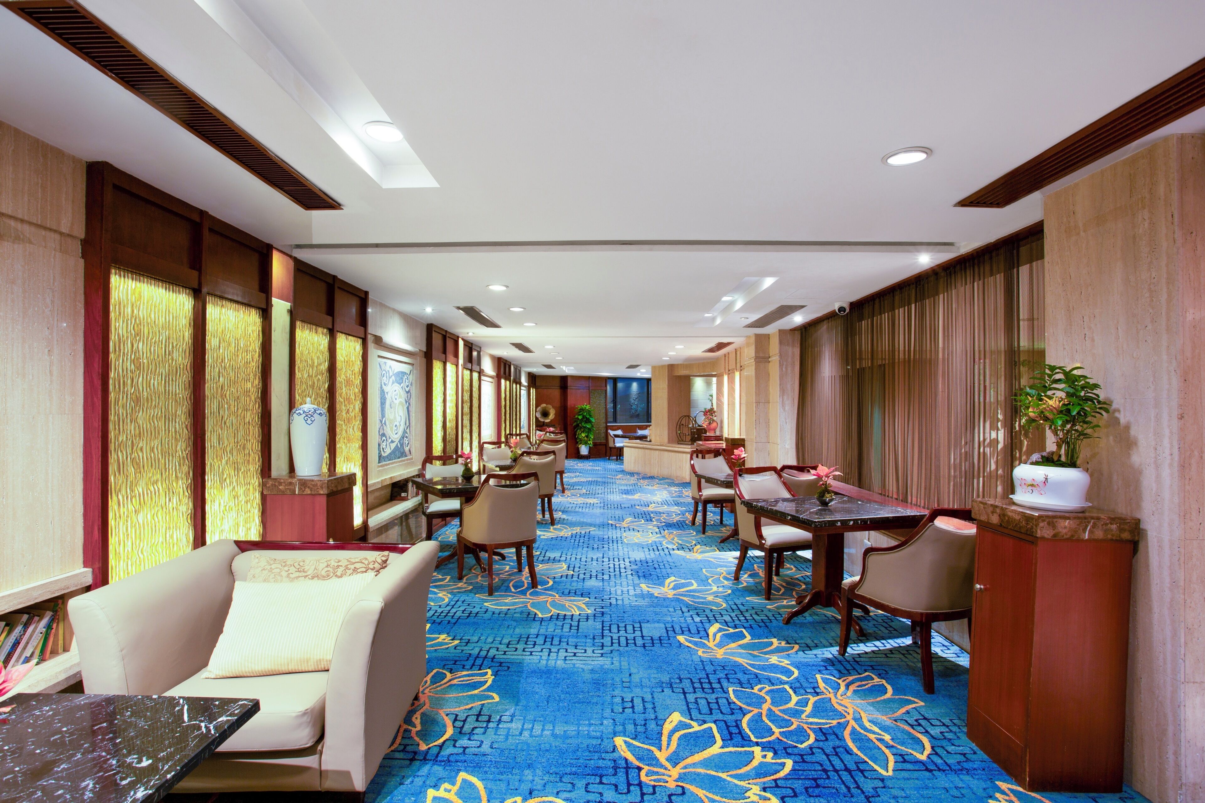 A hotel lobby with a long corridor, seating areas, and a reception desk.