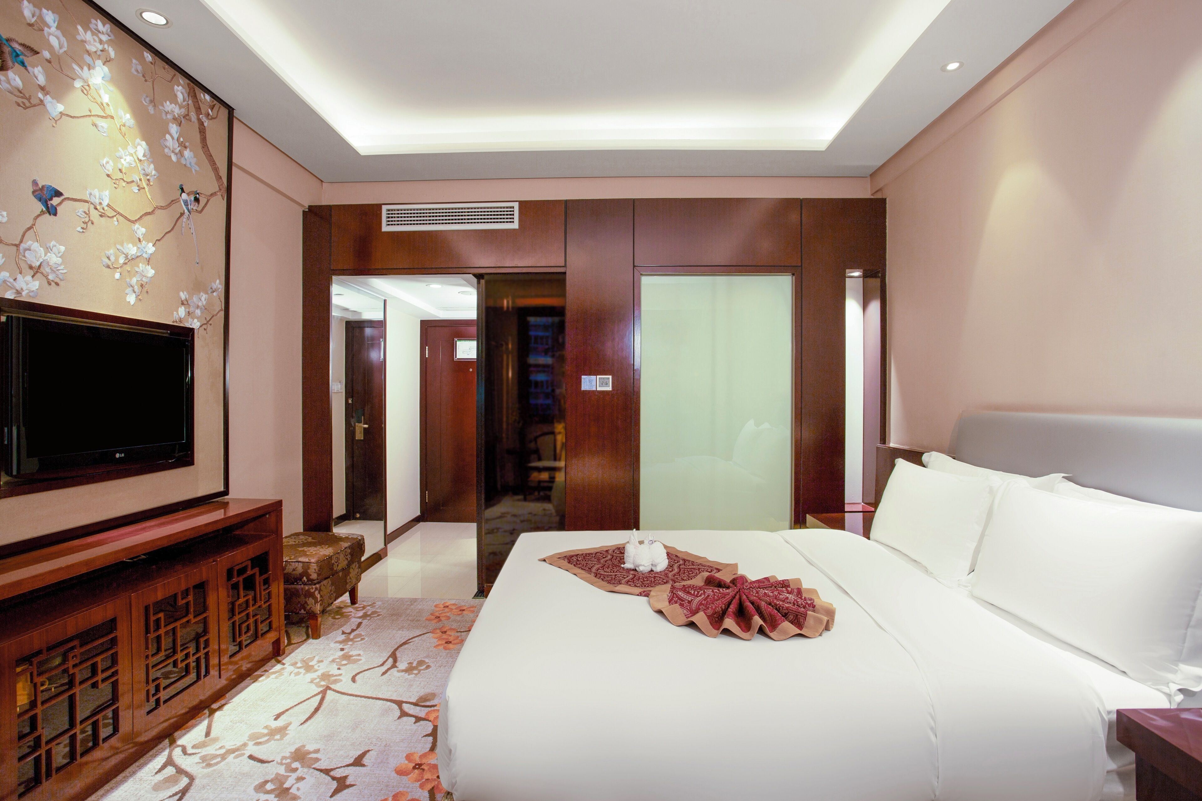 Une chambre d’hôtel avec un grand lit, un téléviseur à écran plat, une armoire en bois et un mur décoratif.