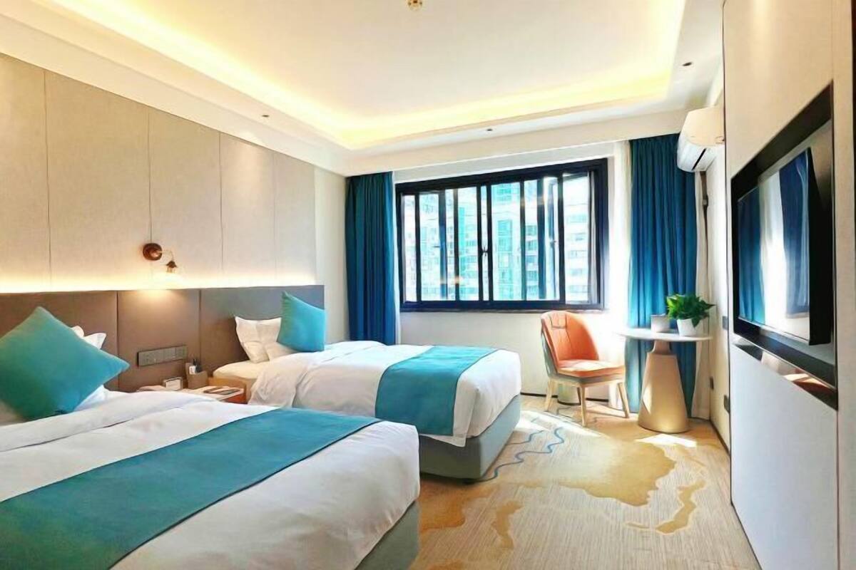 Une chambre d’hôtel avec deux lits, un bureau, une chaise, une télévision et une grande fenêtre.