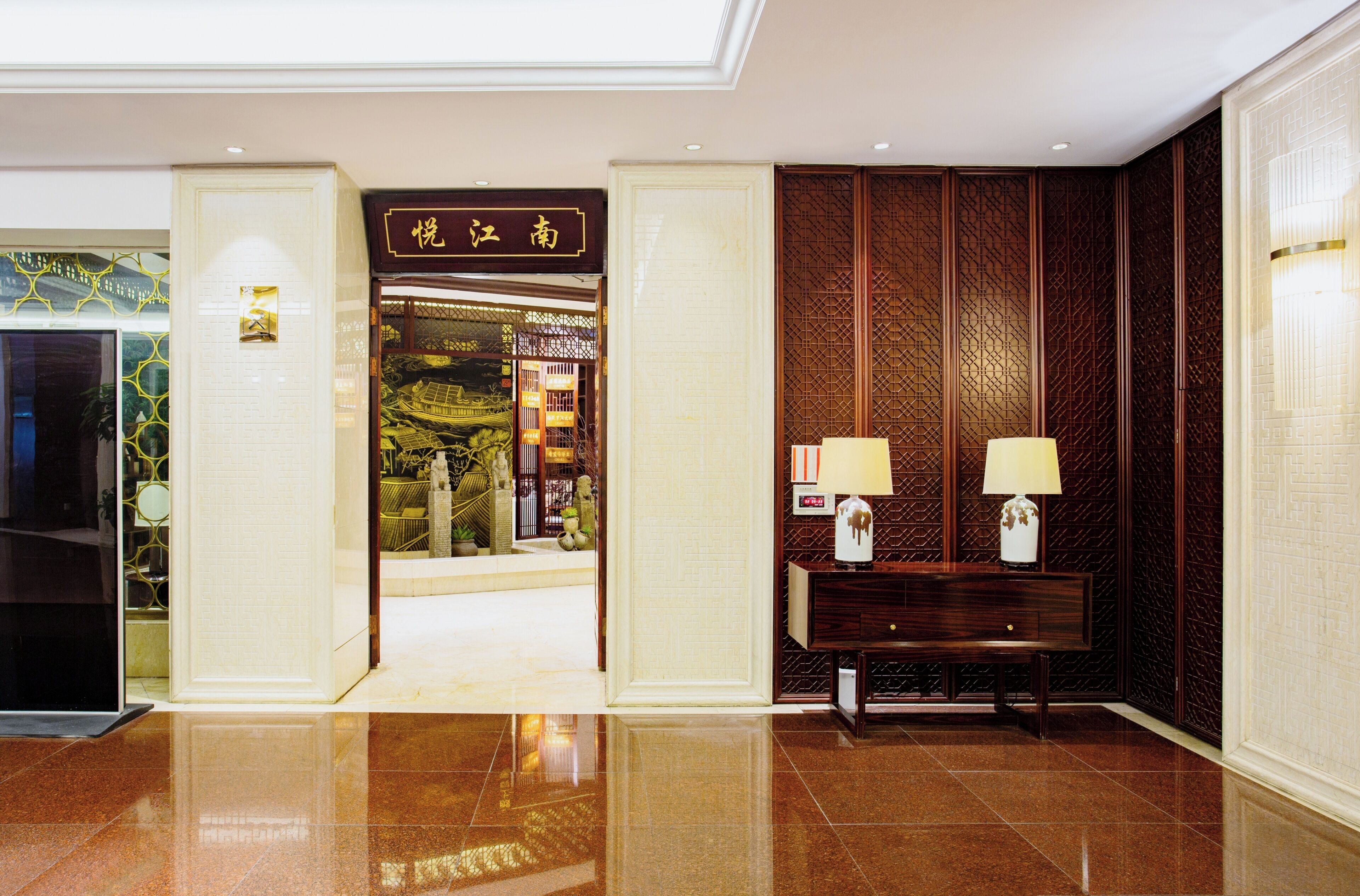 A hotel lobby with a polished floor, a reception desk, and a traditional Chinese decorative wall.