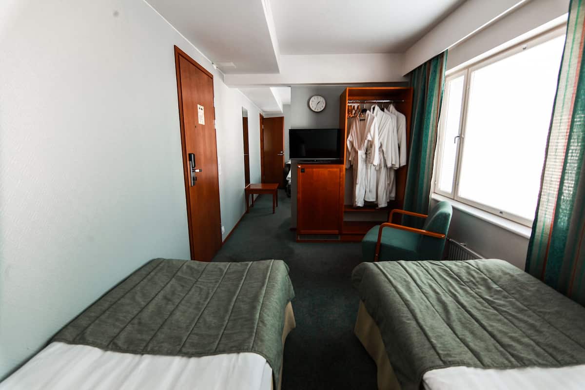 Habitación de hotel con dos camas individuales, televisión, armario y ventana con cortinas.