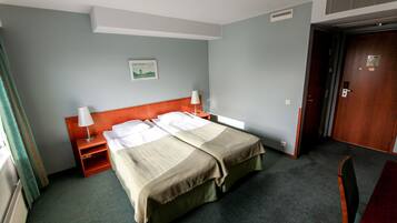 A hotel room with a single bed, a nightstand, a chair, and a door.