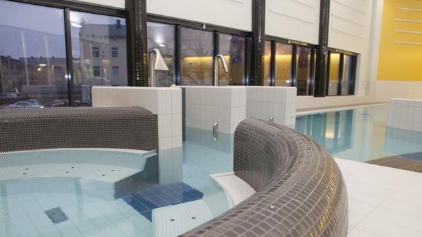An indoor swimming pool with tiled walls and a curved seating area.