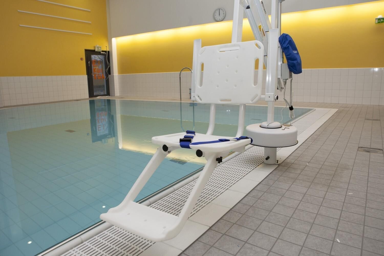 A swimming pool with a starting block, a lifeguard chair, and a clock on the wall.