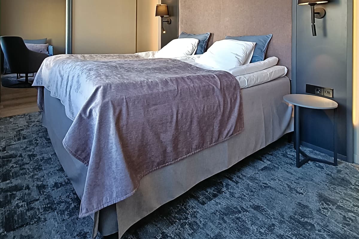 Una habitación de hotel moderna con una cama grande, dos mesitas de noche con lámparas, una silla y una lámpara de techo.