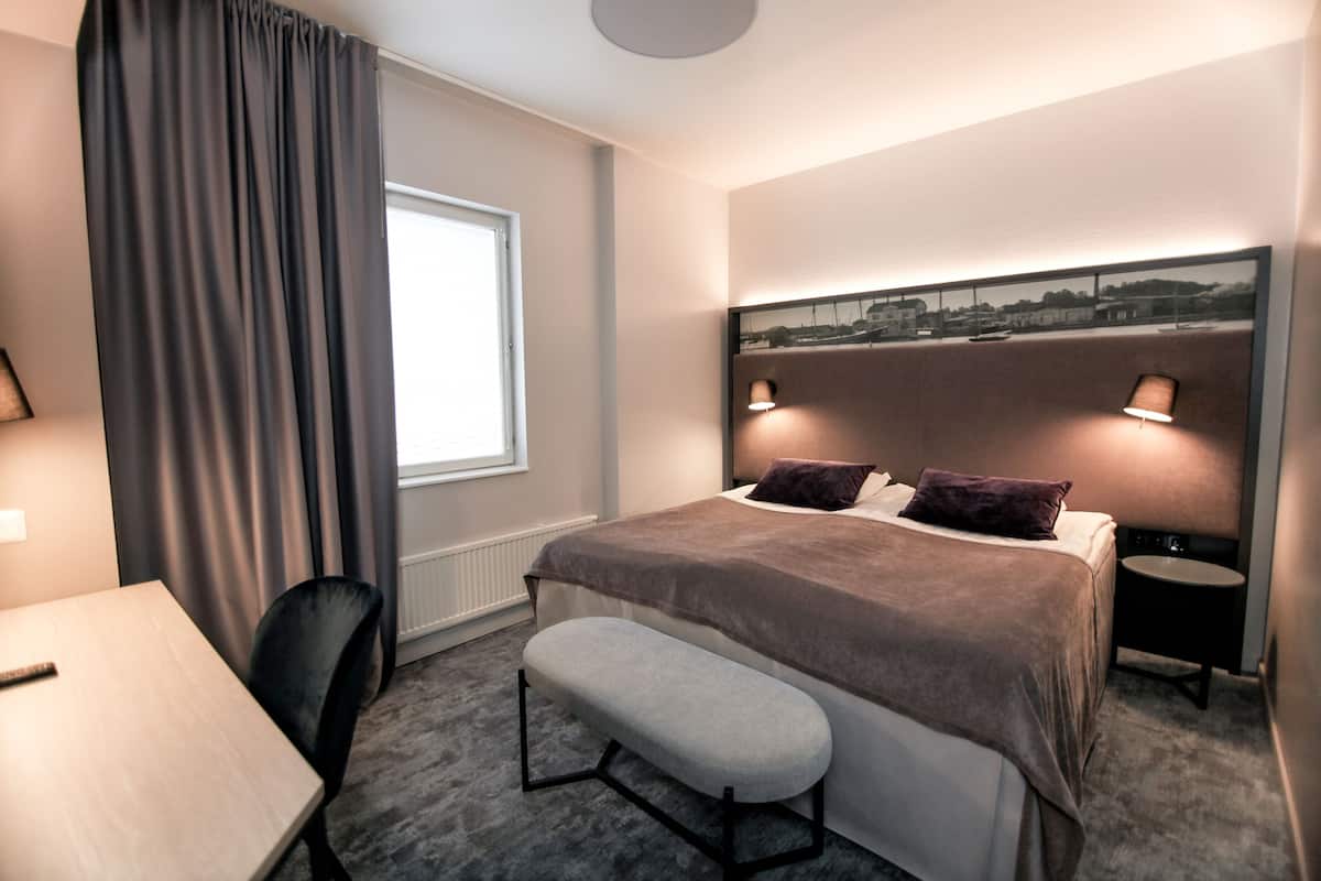 Una habitación de hotel con una cama, lámparas de noche, un banco, una mesa y una silla.