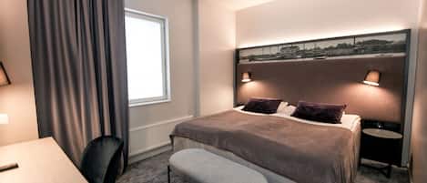 A hotel room with a bed, bedside lamps, a bench, a table, and a chair.