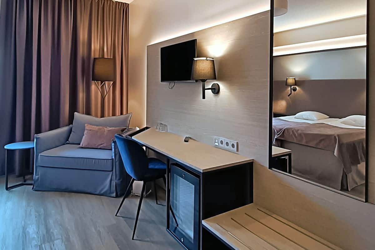 Una habitación de hotel moderna con sofá, escritorio, silla, televisor de pantalla plana y un espejo grande.