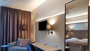 Una habitación de hotel moderna con sofá, escritorio, silla, televisor de pantalla plana y un espejo grande.