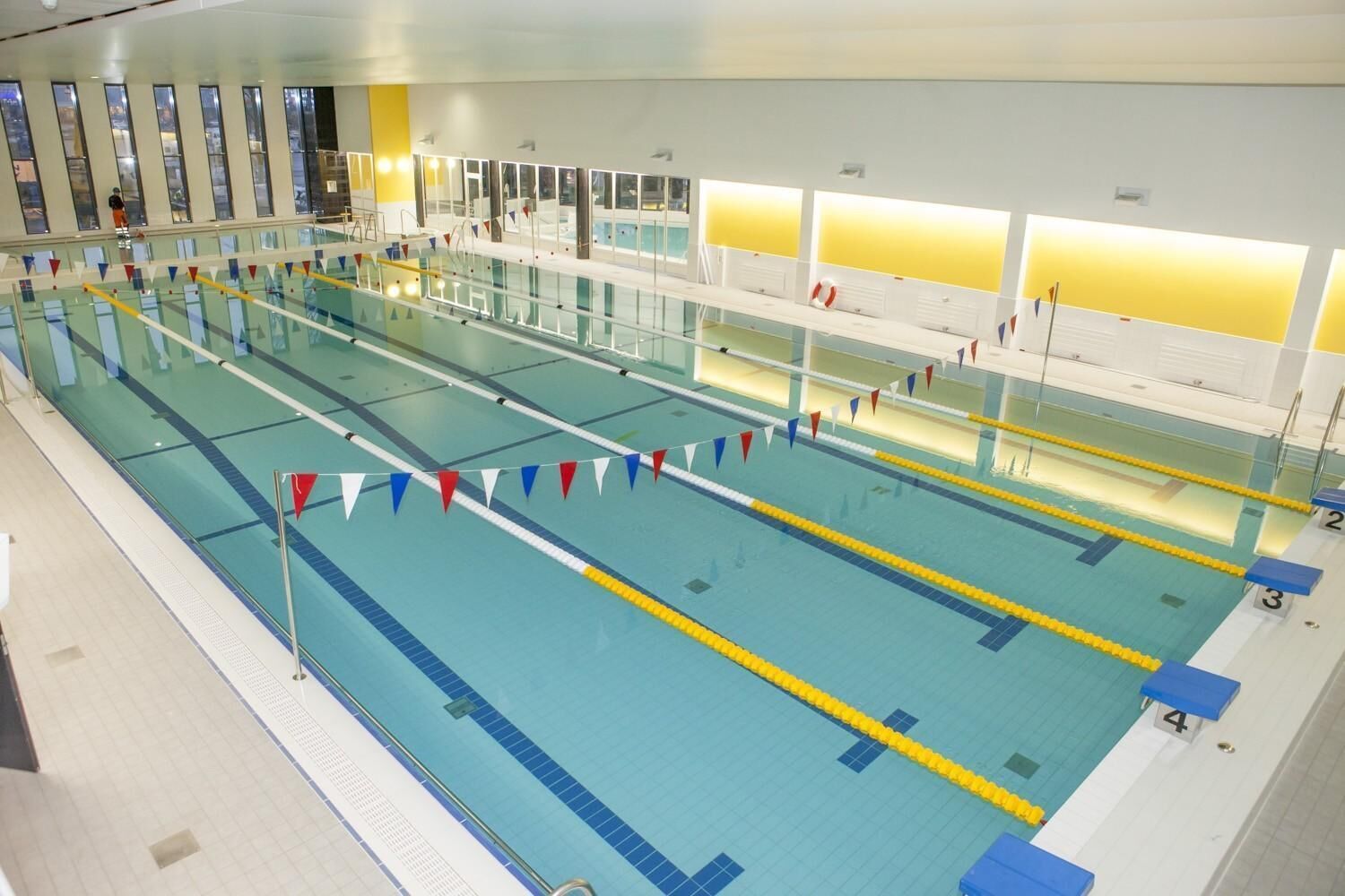 Une grande piscine intérieure dotée de plusieurs couloirs de nage, délimités par des marquages au sol et comportant des plots de départ numérotés.