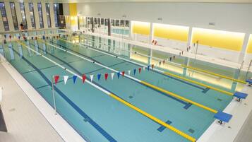 Une grande piscine intérieure dotée de plusieurs couloirs de nage, délimités par des marquages au sol et comportant des plots de départ numérotés.